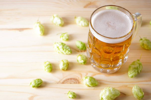 Легкое пиво в стакане и хмелевые шишки на деревянном фоне. - Фото, изображение