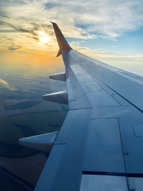 View from airplane window and the wing with sunset sky over fluffy clouds, flying and traveling concept background - Foto, Imagen