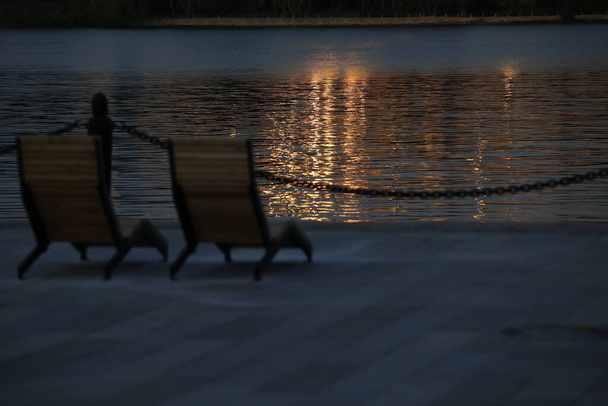 Two chairs on the dock at dusk against a shimmering Golden wave.Beautiful sunset landscape by the water.Focus on water - Valokuva, kuva