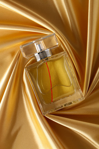 Perfume bottle on Golden silk folded fabric background. Glass flask with dark Gold liquid.Scent fragrance cosmetic beauty product. - Photo, image
