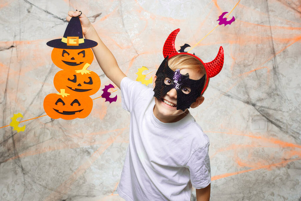 een kind met een masker en hoorns op zijn hoofd speelt met een Halloween pompoen - Foto, afbeelding