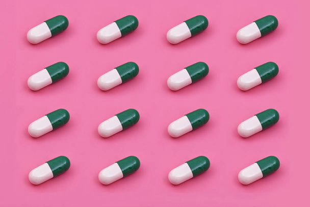 Capsule blanche verte Comprimé pharmaceutique sur fond rose, concepts créatifs de médecine. Style minimal avec fond en papier coloré.Couleurs à la mode, Modèle tendance - Photo, image