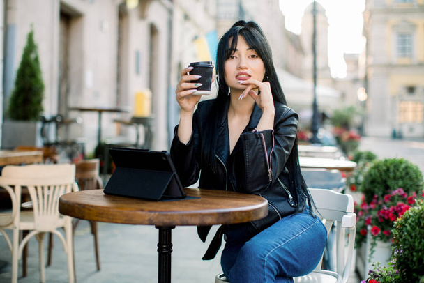 Lifestyle freelance concept. Pretty working young Asian woman with tablet computer, drinking coffee in outdoor city coffee cafe shop, working online, reading news and enjoying coffee break - Fotografie, Obrázek