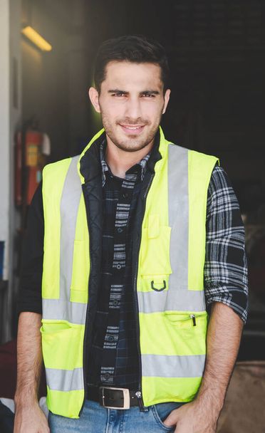 Ritratto di un ingegnere di fabbrica in uniforme in piedi all'interno della fabbrica. Un operaio caucasico sorride mentre sta in piedi nel tempo di riposo della vita di fabbrica. - Foto, immagini