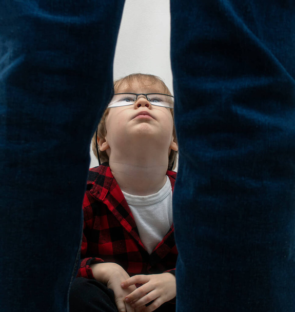 A little boy with glasses is sitting and looking up at the standing man in dismay. Domestic violence, kidnapping and child abuse concept - Fotografie, Obrázek