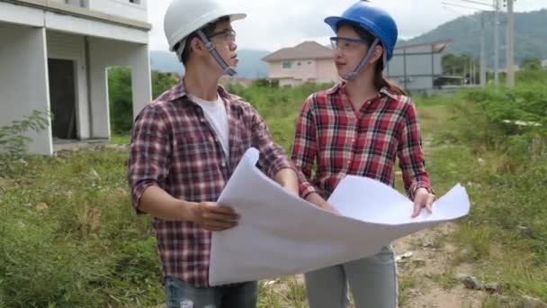 Langzame beelden van het controleren van de bouwplaats, Aziatische ingenieurs in helmen lopen rond de bouwplaats en controleren met blauwdrukken - Video