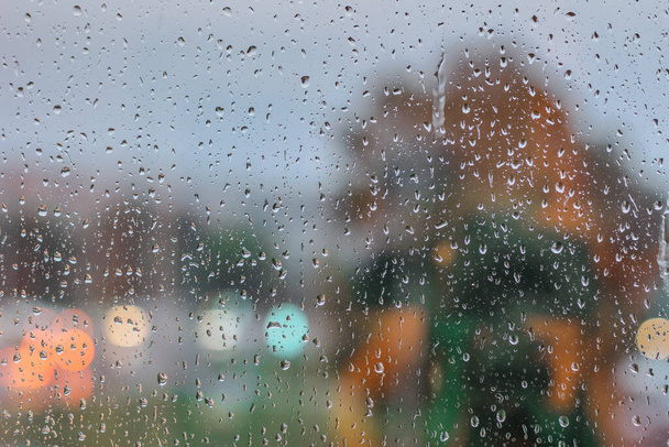 Üvegre csepeg esős időben. Esik az eső a város ablakán kívül. Esőcseppek, nedves üveg. Esős az ablak háttere.Városi közlekedési lámpák az ablakon keresztül egy esős este. Itthon maradni. - Fotó, kép