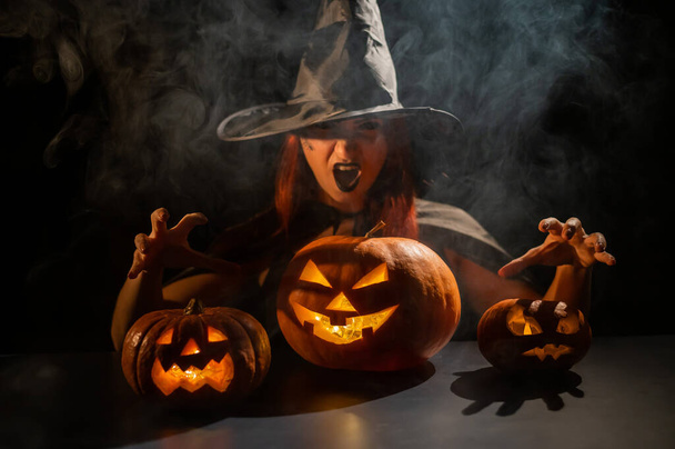 The evil witch casts a spell on pumpkins. Portrait of a woman in a carnival halloween costume in the dark - Fotoğraf, Görsel