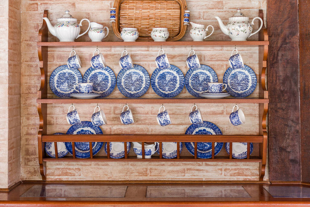 Набір біло-блакитного посуду добре організований в дерев'яних меблях в цегляній задній стіні
 - Фото, зображення