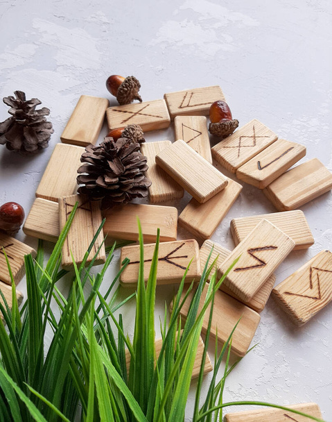 Runes made of wood on a gray background with bunches of green grass - Фото, зображення