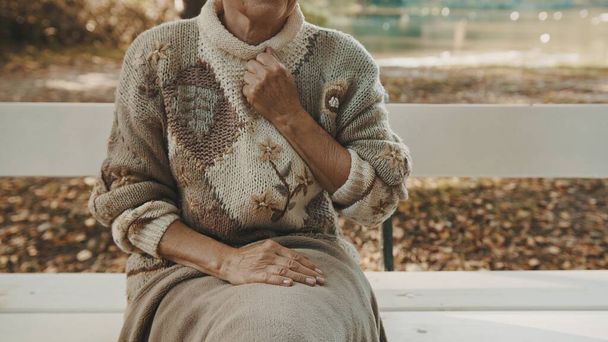Starsza kobieta z pięścią nad klatką piersiową w bólu, siedząca jesienią na ławce w parku - Zdjęcie, obraz