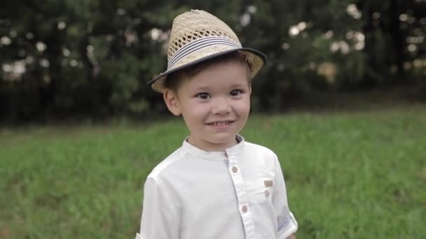 Χαμογελώντας ντροπαλό Καυκάσιο παιδί με ψάθινο καπέλο κοιτώντας μπροστά - Πλάνα, βίντεο