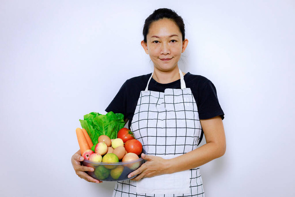 Ασιάτισσα γυναίκα στέκεται χαμόγελο και κρατώντας μίγμα νωπών λαχανικών κουτί. Αρχική κουζίνα και σπιτικό φαγητό Concept. Ένα πρόσωπο που ψάχνει κάμερα με αντιγραφή χώρο εσωτερική μπροστινή όψη με απομονωμένο λευκό φόντο. - Φωτογραφία, εικόνα