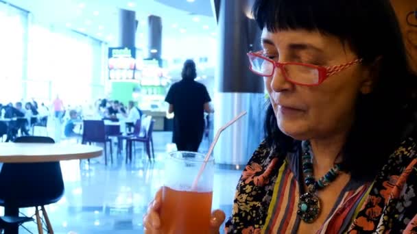 Mature adult woman drinks fruit juice through straw in cafe or restaurant on food court in mall. Close-up. - Footage, Video