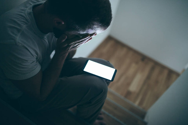 Depressed man sitting in the dark with his smartphone - Foto, Imagem