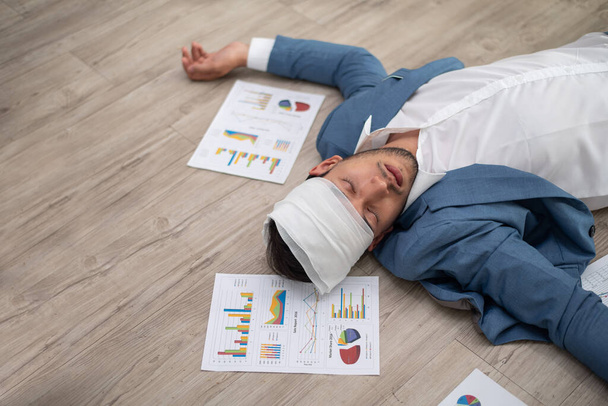 Egy öltönyös üzletember eszméletlenül fekszik a padlón pénzügyi jelentésekkel az irodában. - Fotó, kép