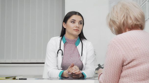 Giovane medico femminile che ascolta il suo paziente anziano durante un appuntamento medico - Foto, immagini
