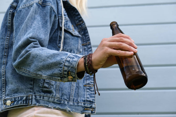 A brown bottle of beer in a hand of punk, informal woman, alcohol addiction, overdosage and abuse concept. - Фото, изображение