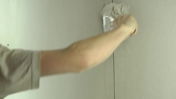 A munkás egy spatulával vakolja a falat, és betonkeveréket alkalmaz. A szerelő a gipszet a gipszkartonra helyezi. Az ezermester otthon javít. Munkás lakás helyreállítása.Specialista takarja repedések - Felvétel, videó