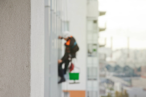 Industrial mountaineering worker hangs over residential building while washing exterior facade glazing. Rope access laborer hangs on wall of house. Concept of urban works. Copy space - Foto, Bild