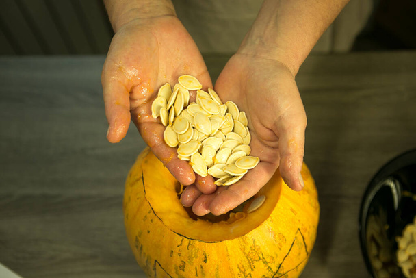 Making Jack O'Lantern at home. Pumpkin preparation process. Women's hands take out seeds from a pumpkin. - Photo, Image