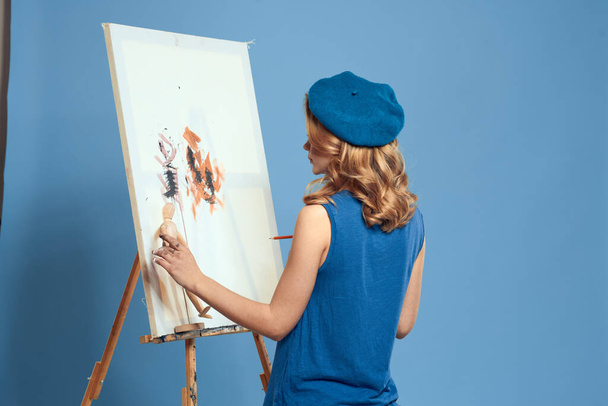Woman artist paintbrush paint on canvas easel art education blue background - Photo, Image