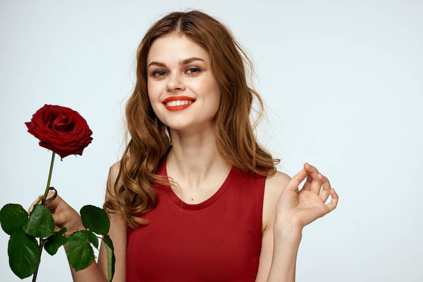 Krásná žena v červených šatech drží růži v ruce dárek květiny dekorace atraktivní vzhled - Fotografie, Obrázek