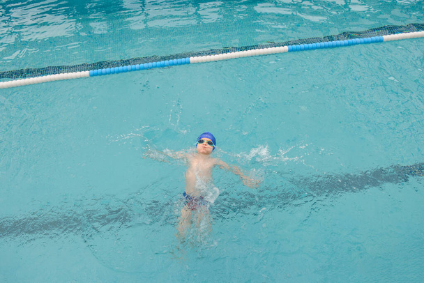 top view of a 7-year boy swimming backstroke in a swimming pool - Fotó, kép