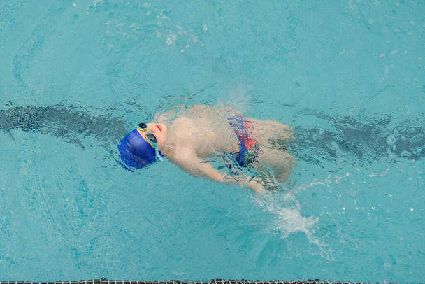 Вид сверху на 7-летнего мальчика, плавающего спиной в бассейне - Фото, изображение