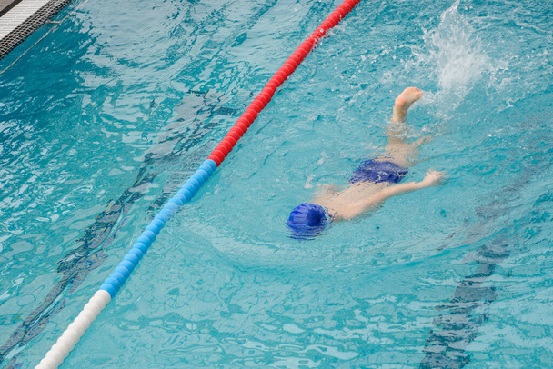 Blick von oben auf einen 7-jährigen Jungen beim Spielen und Schwimmen im Schwimmbad - Foto, Bild