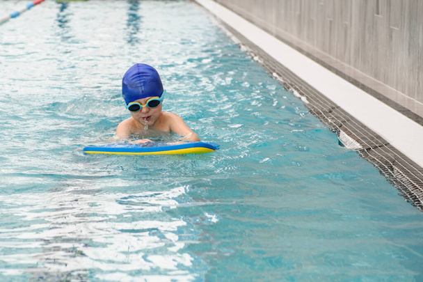 close up photo of 7-year boy swimming with a kickboad in the swiimming pool - Photo, Image