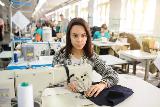close up photo of a young woman sewing with sewing machine in a factory - Photo, Image