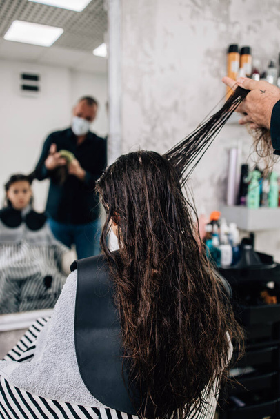 Jeune fille appréciant au traitement de coiffure tandis que le coiffeur professionnel travaille doucement et coupe ses cheveux. - Photo, image
