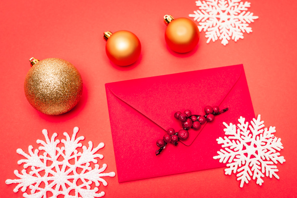 bovenaanzicht van sneeuwvlok, kerstballen en enveloppe op rode achtergrond - Foto, afbeelding