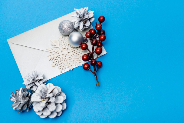 top view of snowflake, silver baubles, berries and envelope on blue background - Fotó, kép