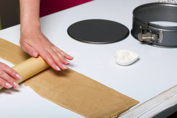 Die Frau rollt den Teig aus. Kochutensilien sind in der Nähe. Levington-Kuchen, Vorbereitungsphase. - Foto, Bild