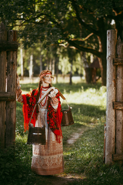 Beautiful Slavic girl with long blonde hair and brown eyes in a white and red embroidered suit and a yoke on her shoulders.Traditional clothing of the Ukrainian region.summer day - Φωτογραφία, εικόνα