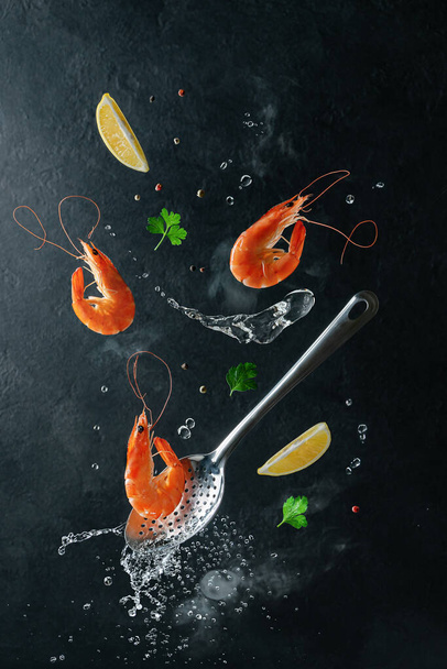 Crevettes tigrées volantes avec des ingrédients sur écumeur et eau bouillie sur fond sombre. Cuisine de fruits de mer - Photo, image