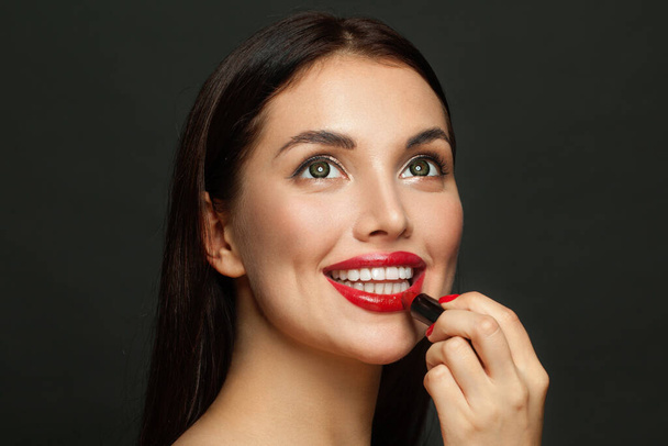 Atractiva cara de mujer con labios rojos y lápiz labial de cerca sobre fondo negro - Foto, Imagen
