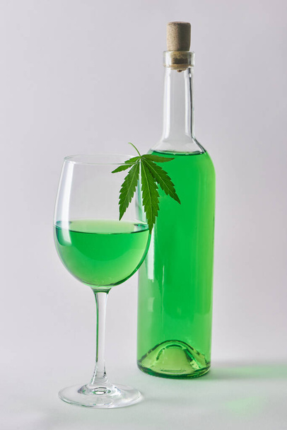 A glass and a bottle of green hemp-infused wine on white background - Foto, Bild