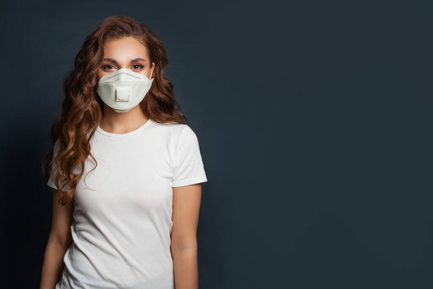 Gelukkig vrouw dragen beschermende medische masker en wit t-shirt op zwarte achtergrond - Foto, afbeelding