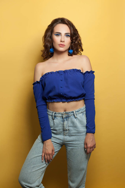 Young woman in blue denim standing on yellow background - Фото, зображення