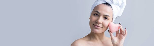 Beauty portrait of woman in white towel on head with a sponge for a body in view of a pink heart. Skincare cleansing eco organic cosmetic spa relax concept. - Photo, image