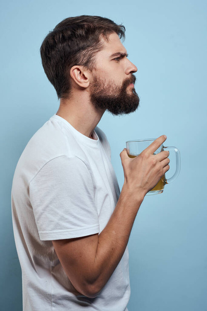 Бородатый мужчина пиво кружка алкоголь белый футболка вид сбоку синий фон - Фото, изображение