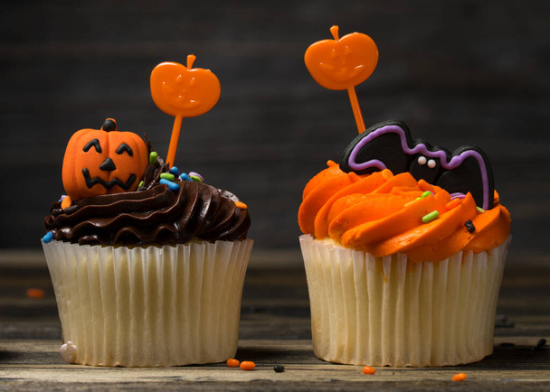Happy Halloween party. Cupcake dessert decorated with colored frosting and Icing shaped pumpkin Jack-o-lantern, ghost and bat. Cupcakes on wooden background.  - Photo, Image