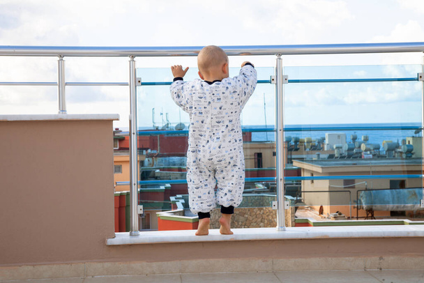 Home Accident. Baby boy pulling glass window on balcony. - Photo, Image