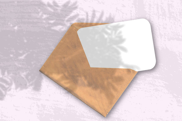 Una busta con due fogli di carta bianca strutturata sullo sfondo rosa. Il Mockup si sovrappone alle ombre delle piante. La luce naturale proietta ombre da un ramo di Rowan. Orientamento orizzontale. - Foto, immagini