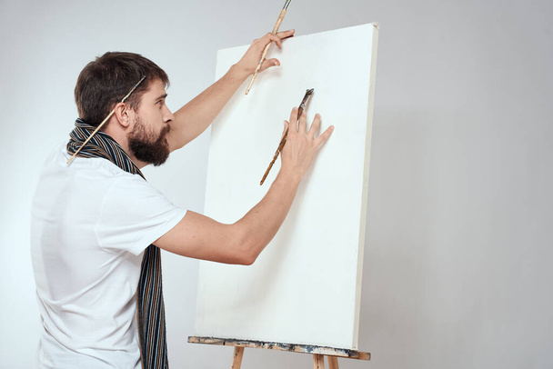 Muž umělec štětec v rukou stojan umění hobby světlo pozadí šála kolem krku - Fotografie, Obrázek