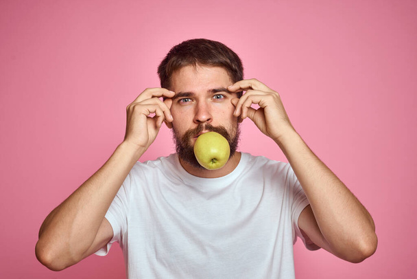 Lindo hombre con una manzana sobre un fondo rosa gestos con las manos recortadas camiseta blanca Copiar espacio - Foto, imagen