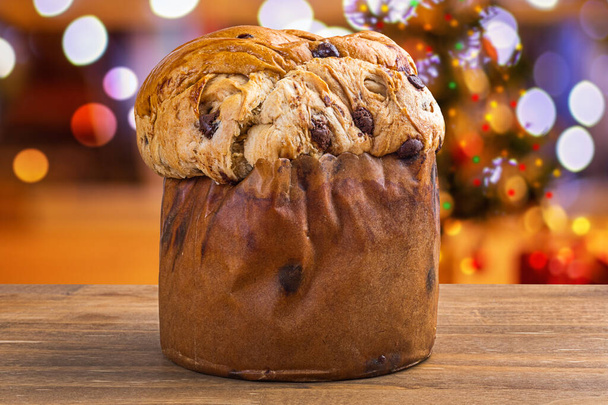 Panettone with chocolate, traditional Italian dessert cake for Christmas. Flashing lights and blurred decorations in the background. - Photo, Image